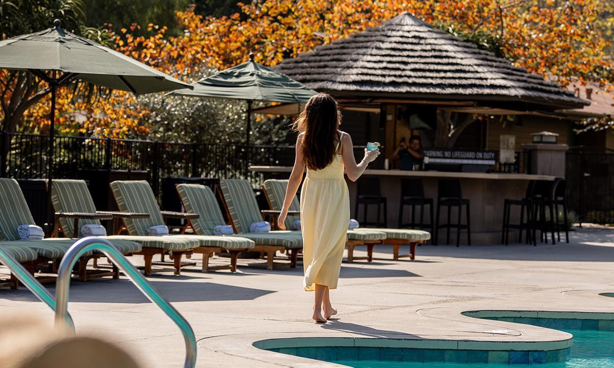 woman walking around pool with a drink